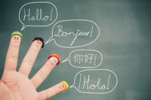 Four smiley fingers on a blackboard saying hello in English, French, Chinese and Spanish.